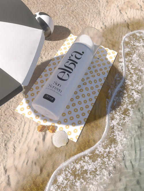 Elara sunscreen bottle on a beach with sand and water in the background